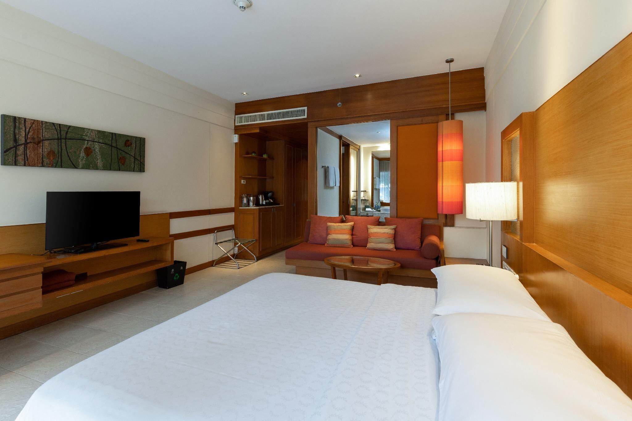 A hotel room with a large bed, a TV, a sofa, and a wooden wardrobe.
