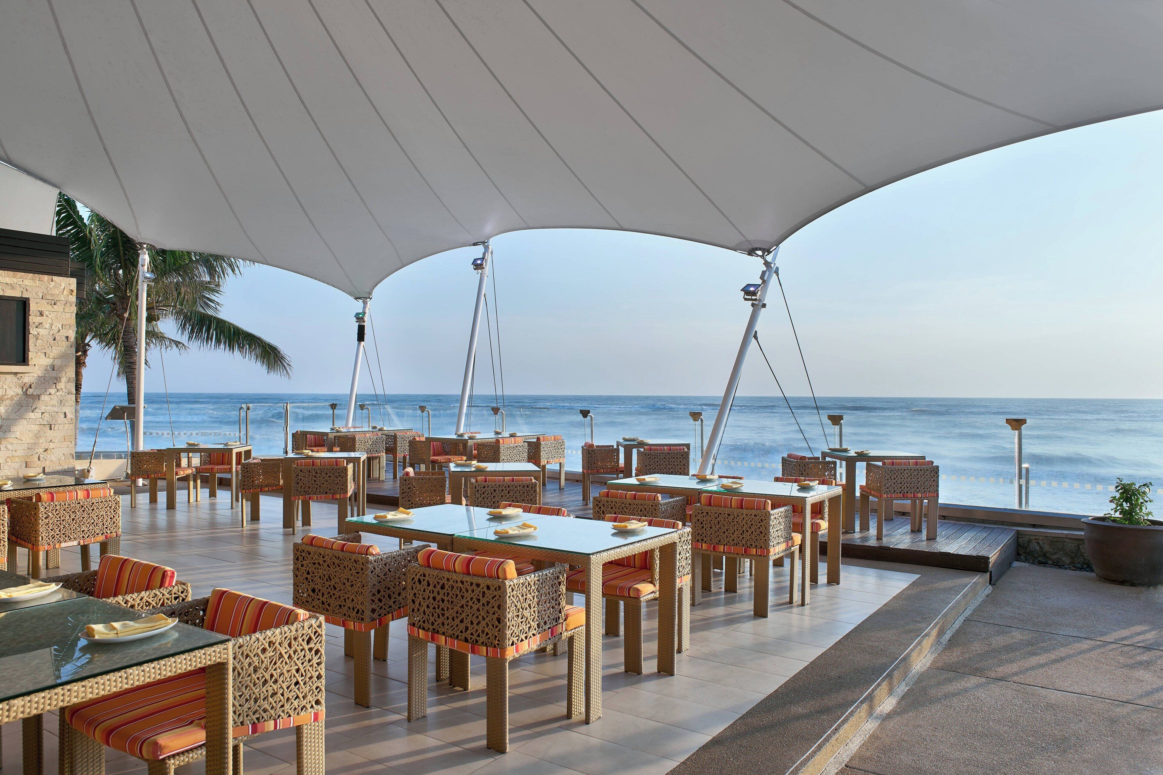 Un área de comedor al aire libre con mesas y sillas, con vista al mar.