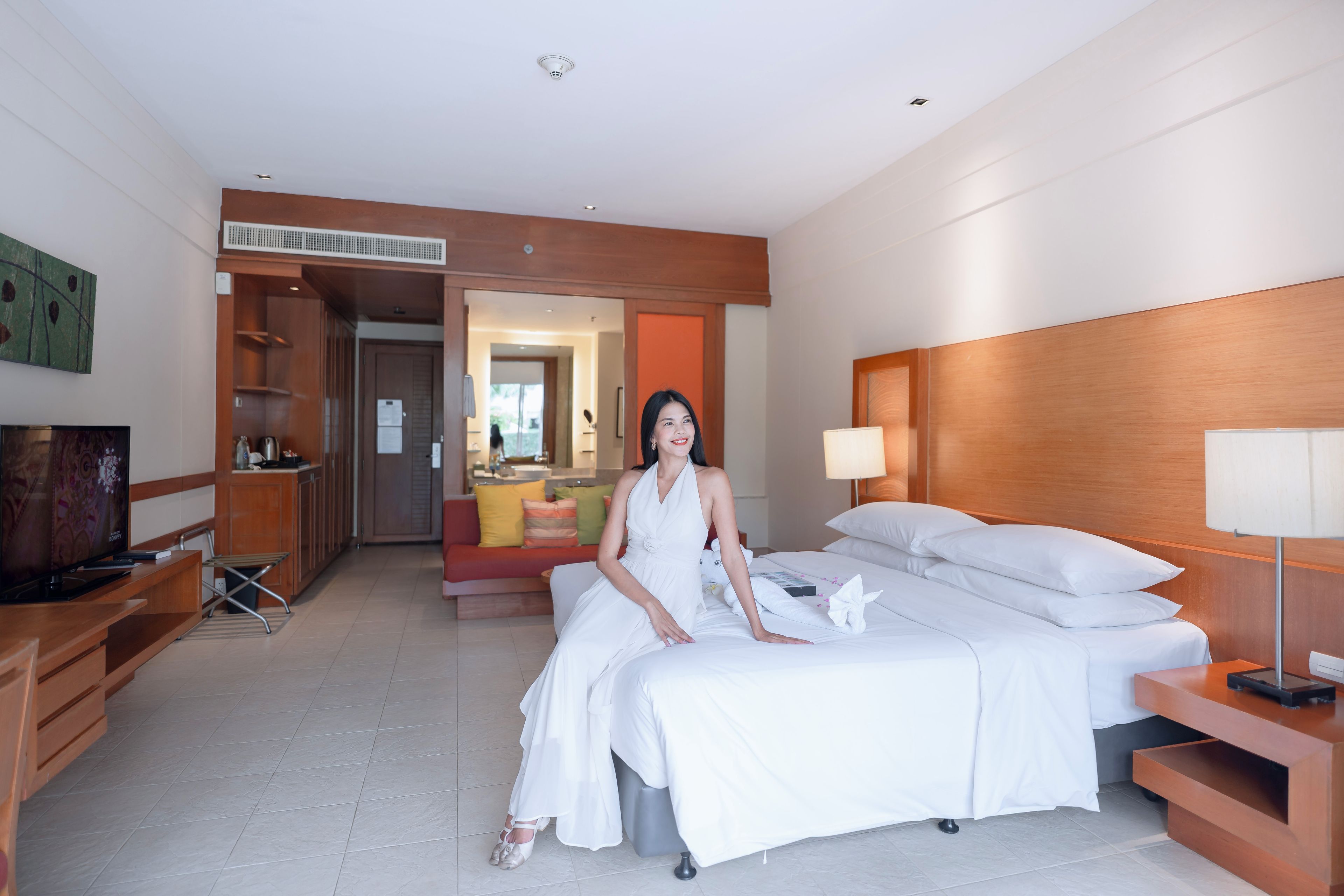 A hotel room with a bed, a TV, a desk, and a bathroom visible through an open door.