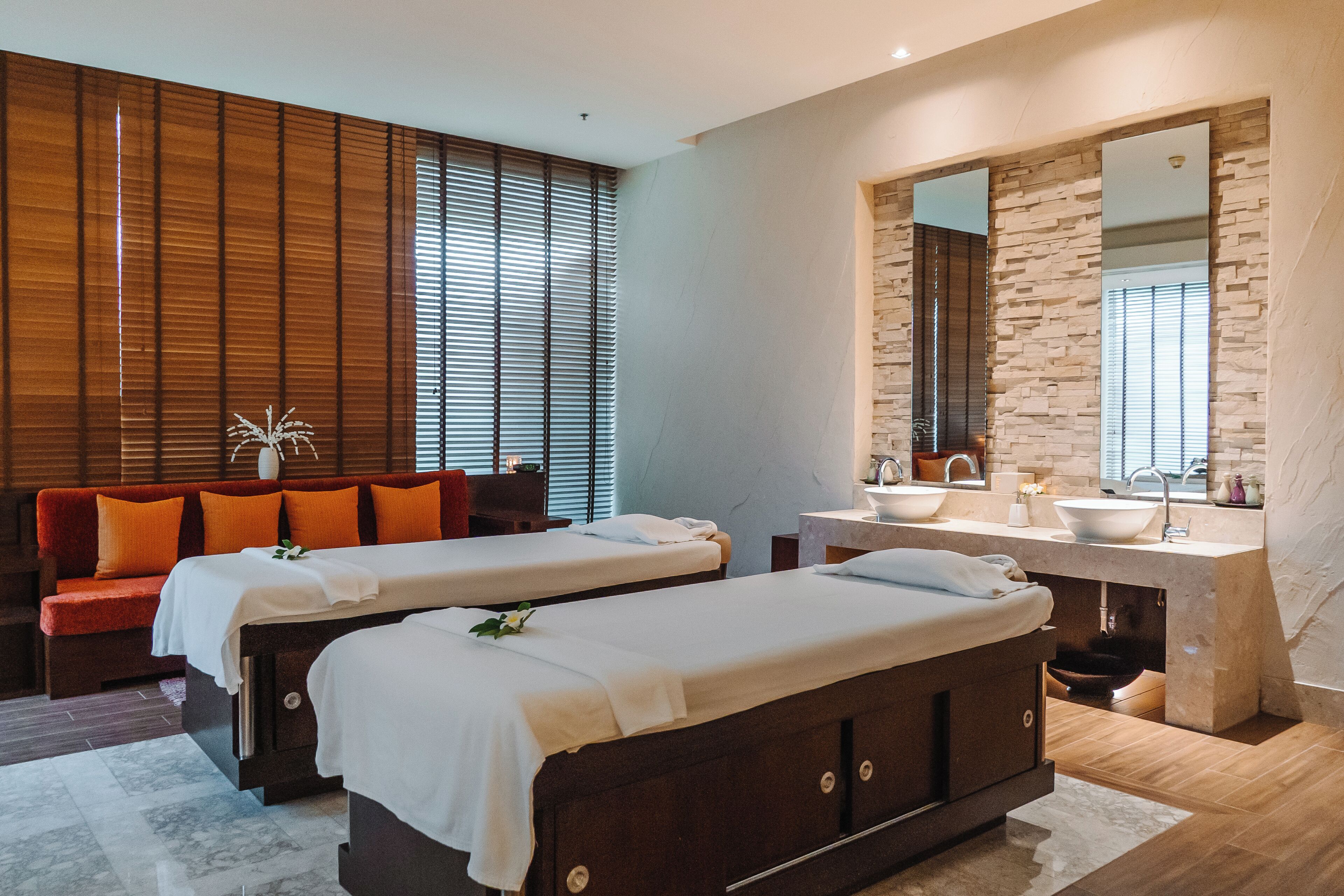 Un spa moderno con dos camillas de masaje, una pared decorada con piedra y un espejo grande sobre el lavabo.