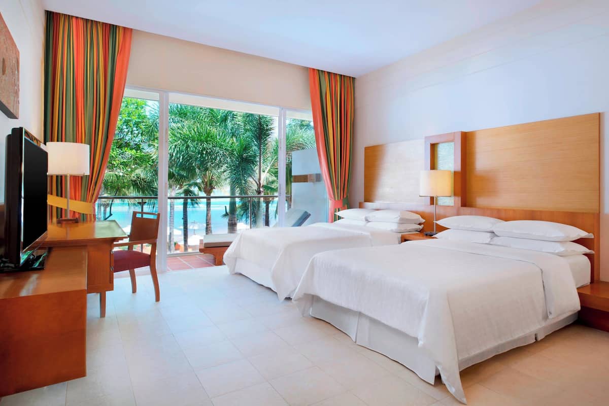 Une chambre d’hôtel avec deux lits, un bureau avec une chaise, une télévision et un balcon avec des rideaux.