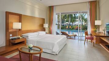 Una camera d'albergo con un letto, comodini, una scrivania, una sedia, un tavolino con un vaso e vista su una piscina e palme all'esterno.
