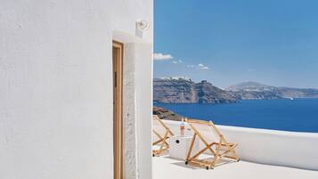 A white building with a door leading to a balcony overlooking a blue sea and distant mountains.