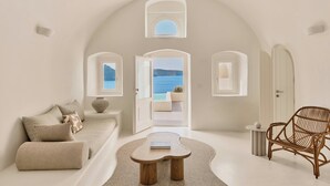 A minimalist room with a sofa, a rattan chair, a small coffee table, and a view of the sea through an open doorway. - Mystique, a Luxury Collection Hotel, Santorini (Santorini)