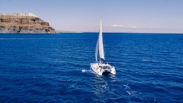 A sailboat on a calm sea with a rocky coastline in the background.