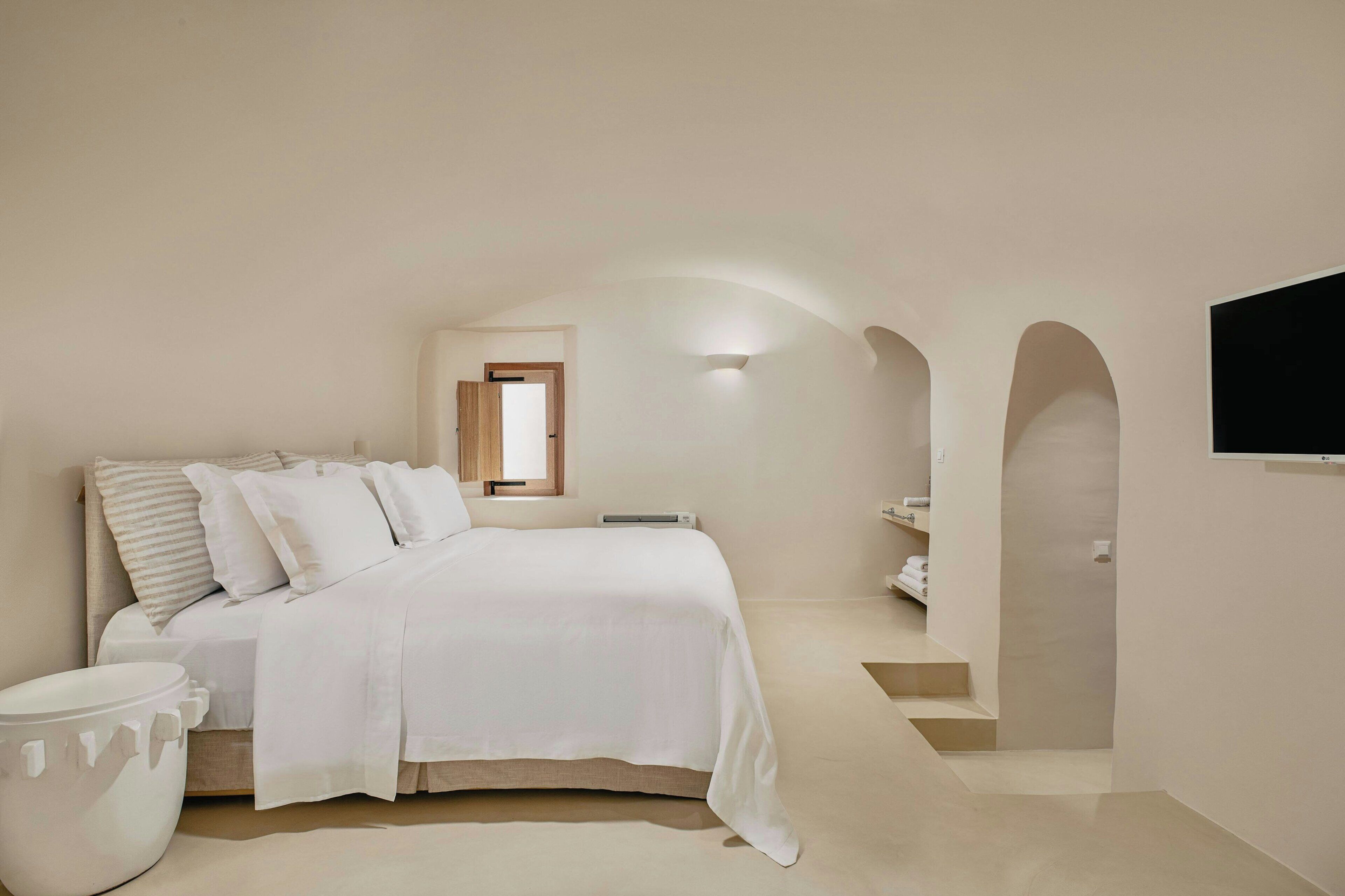 A bedroom with a bed, a bedside table, a TV mounted on the wall, and a window.