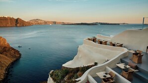 A seaside terrace with outdoor seating overlooking a calm sea and cliffs. - Mystique, a Luxury Collection Hotel, Santorini (Santorini)