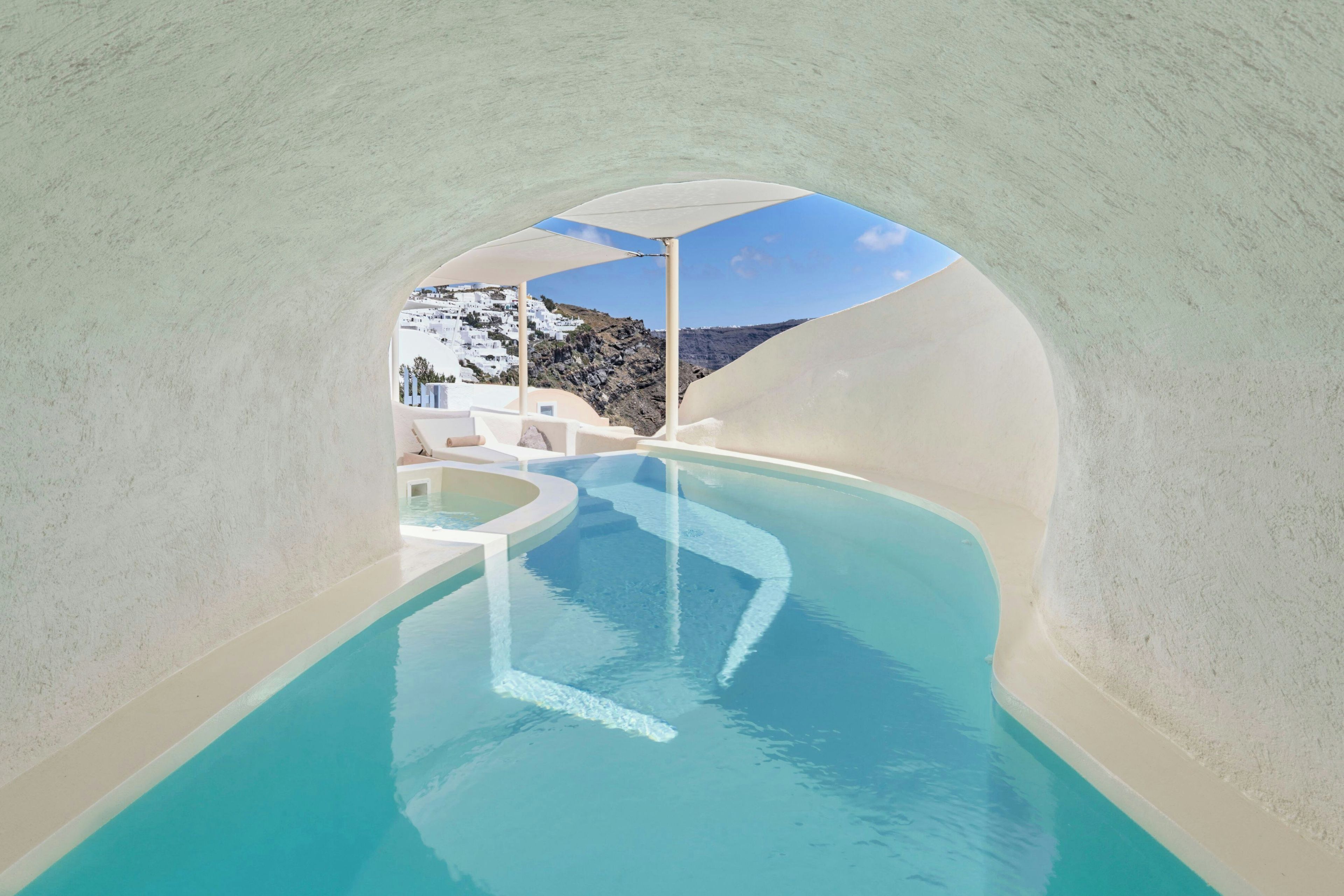 A modern infinity pool with a clear view of a white-washed village and rocky landscape.