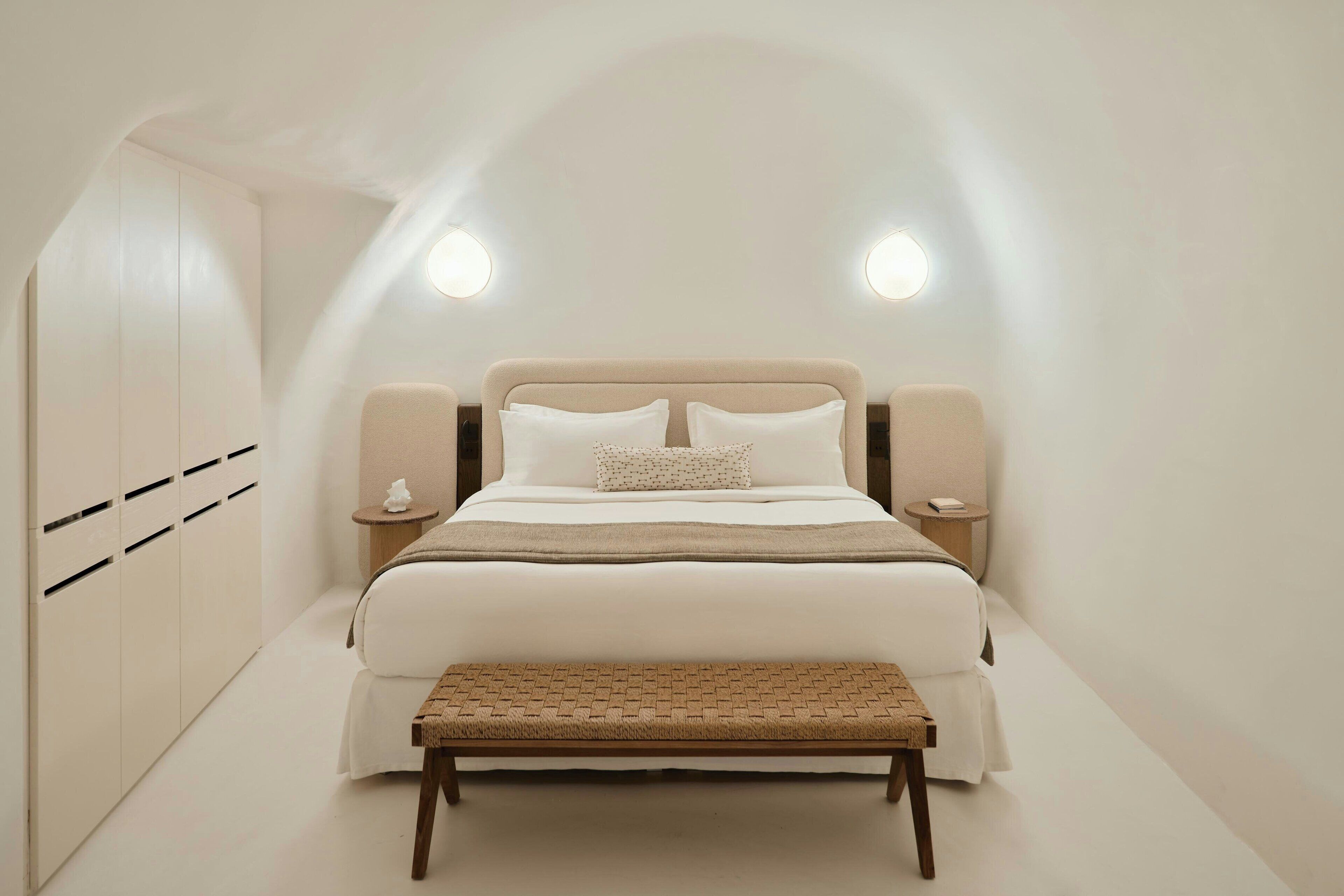 Une chambre à coucher comprenant un lit, des tables de chevet, un banc et une armoire.