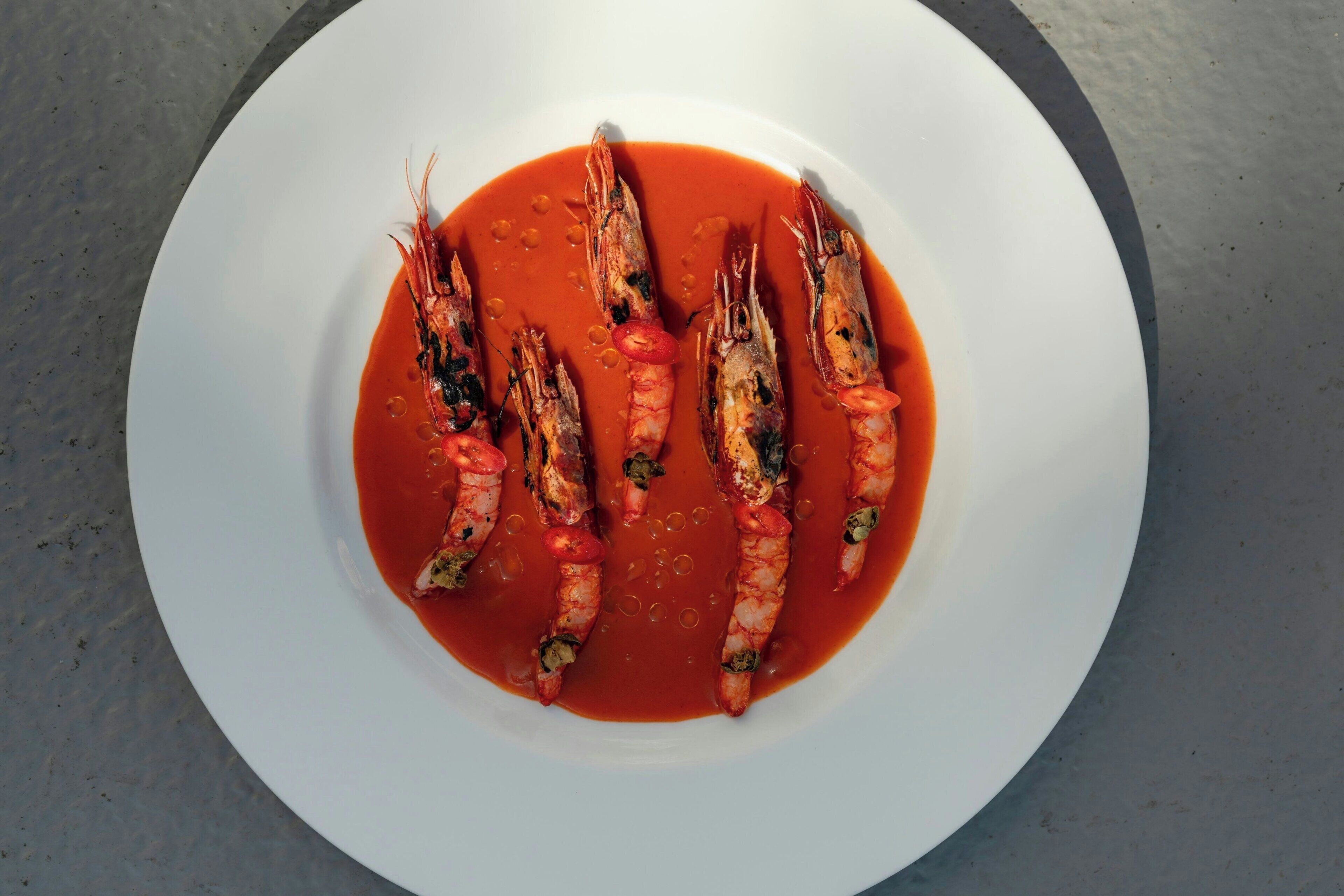 A white plate with cooked shrimp and a red sauce.