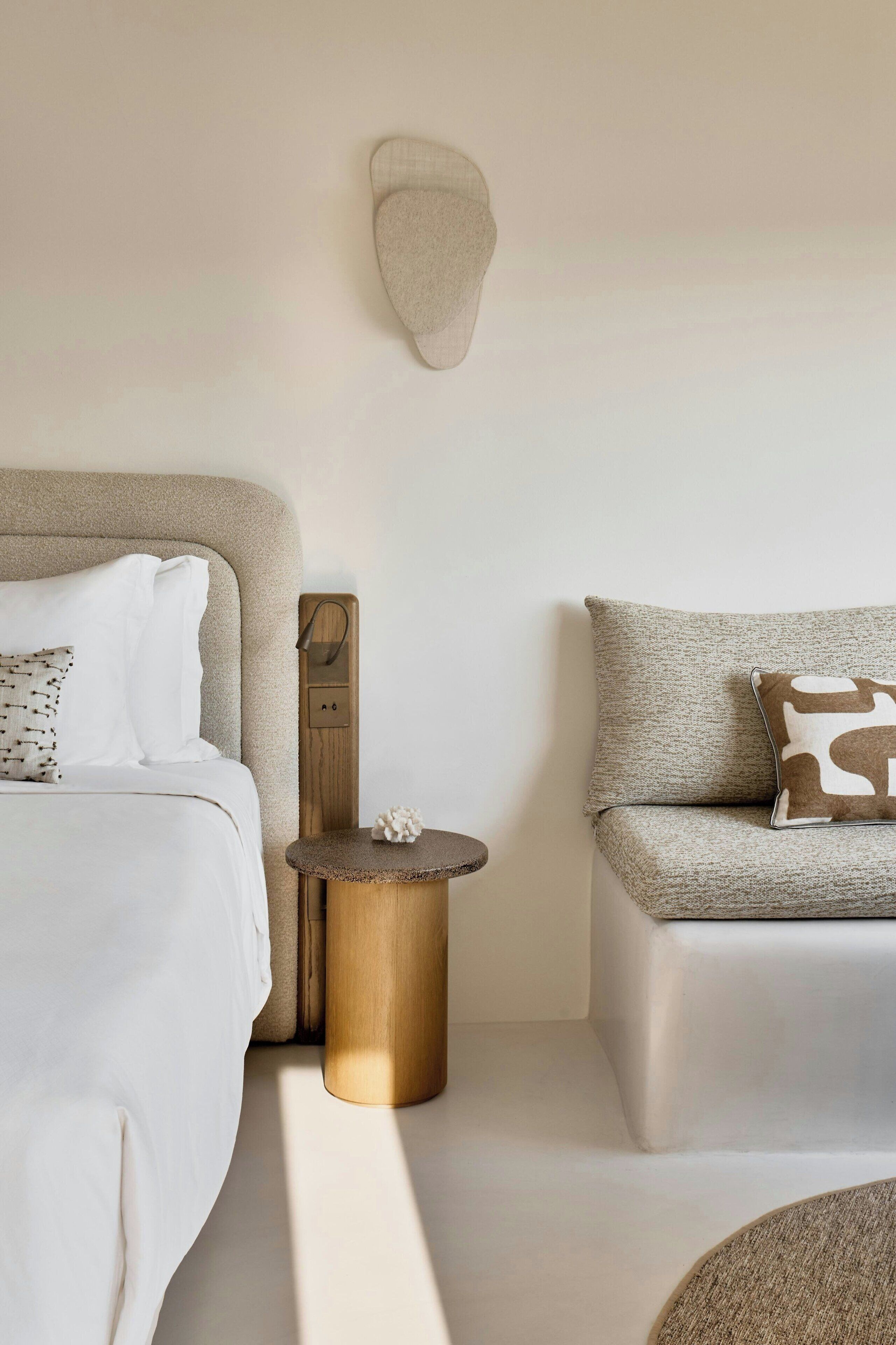 A modern bedroom with a bed, a sofa, a small round table, and a wall-mounted light fixture.