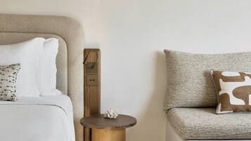 A modern bedroom with a bed, a sofa, a small round table, and a wall-mounted light fixture.
