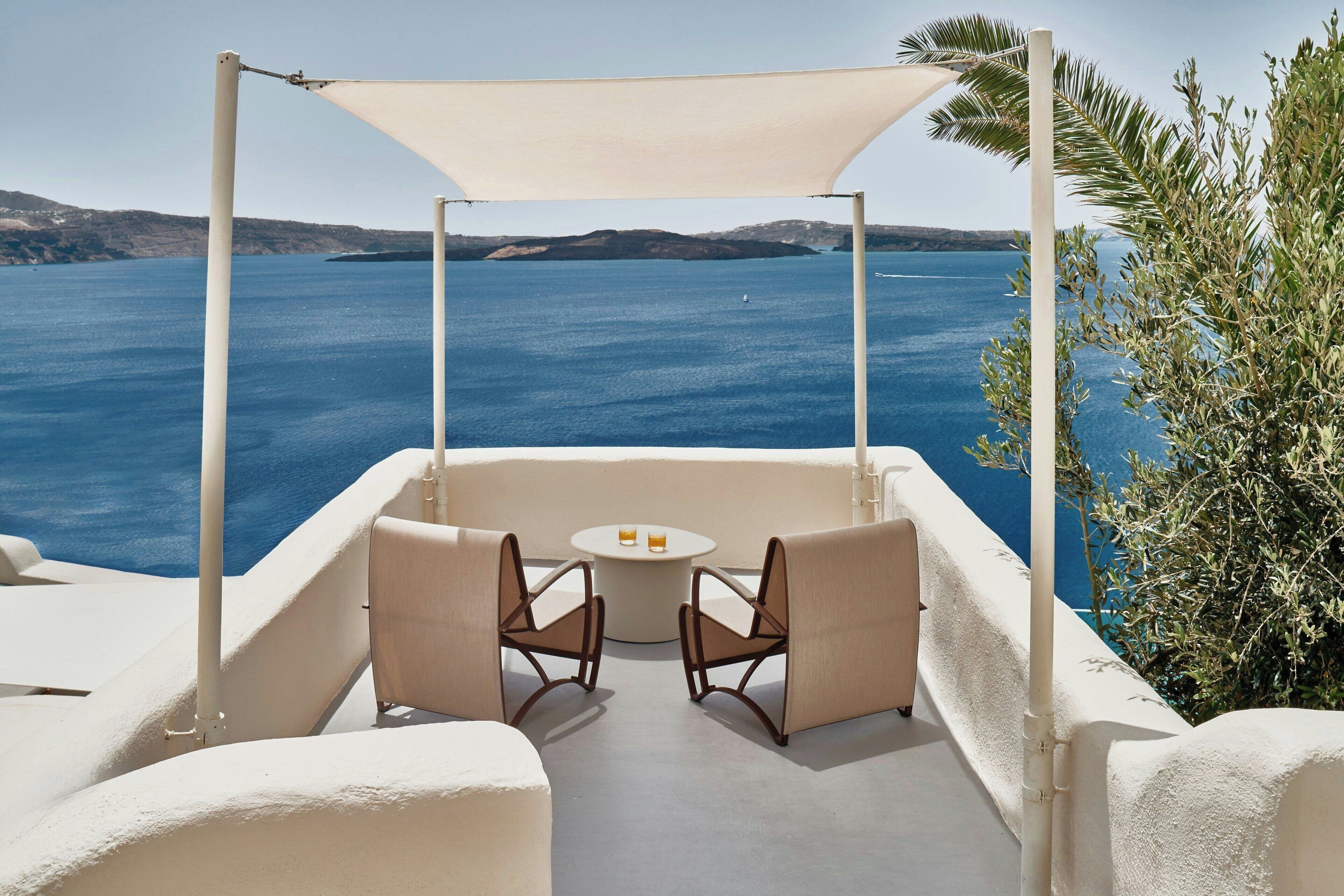 A terrace with two chairs and a table, overlooking a body of water and distant land.