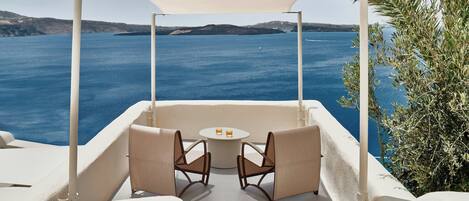 A terrace with two chairs and a table, overlooking a body of water and distant land.