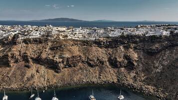 A coastal town with white buildings, a rocky cliff, and several boats anchored near the shore.