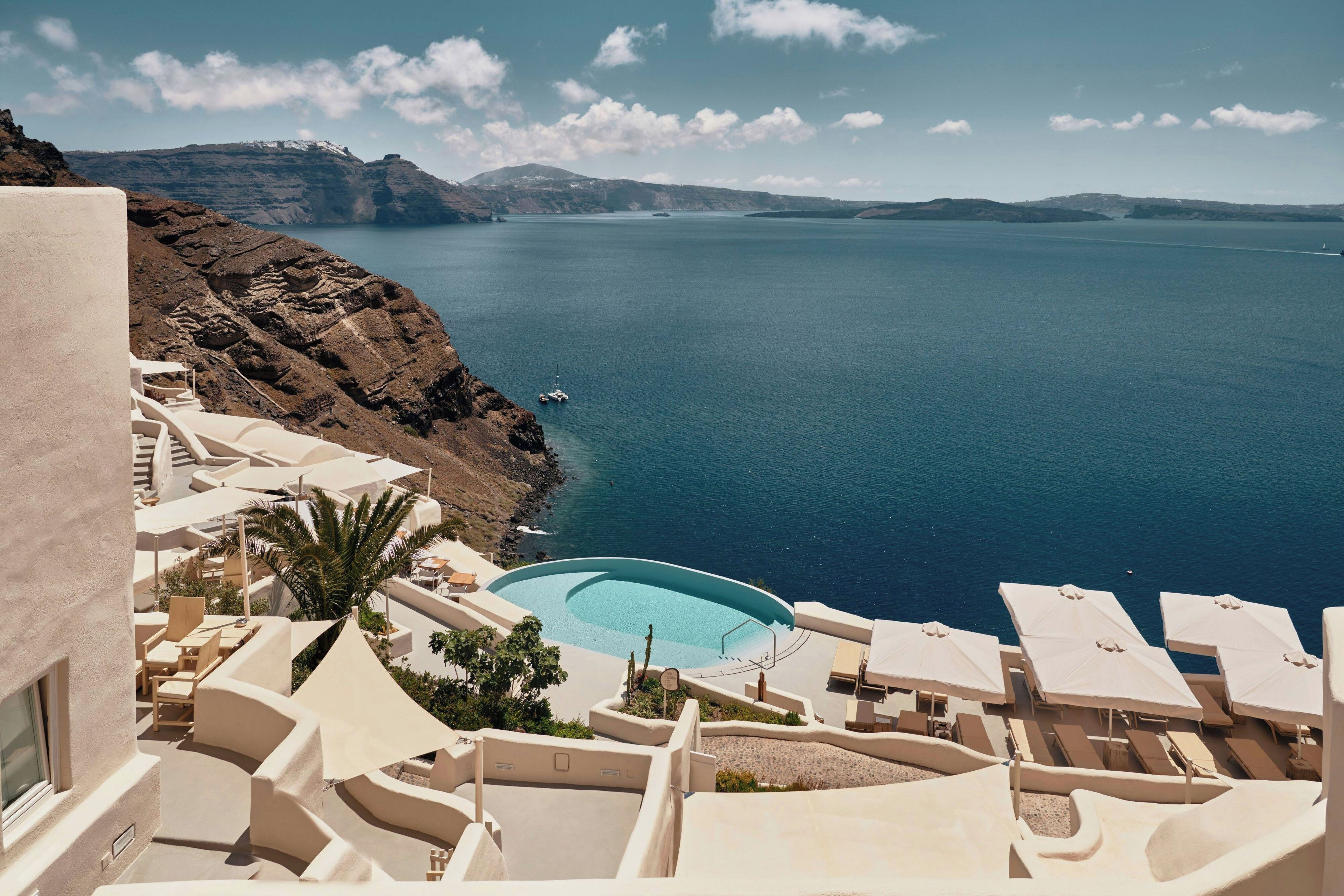 A seaside resort with a pool, lounge chairs, and a view of the sea and mountains.