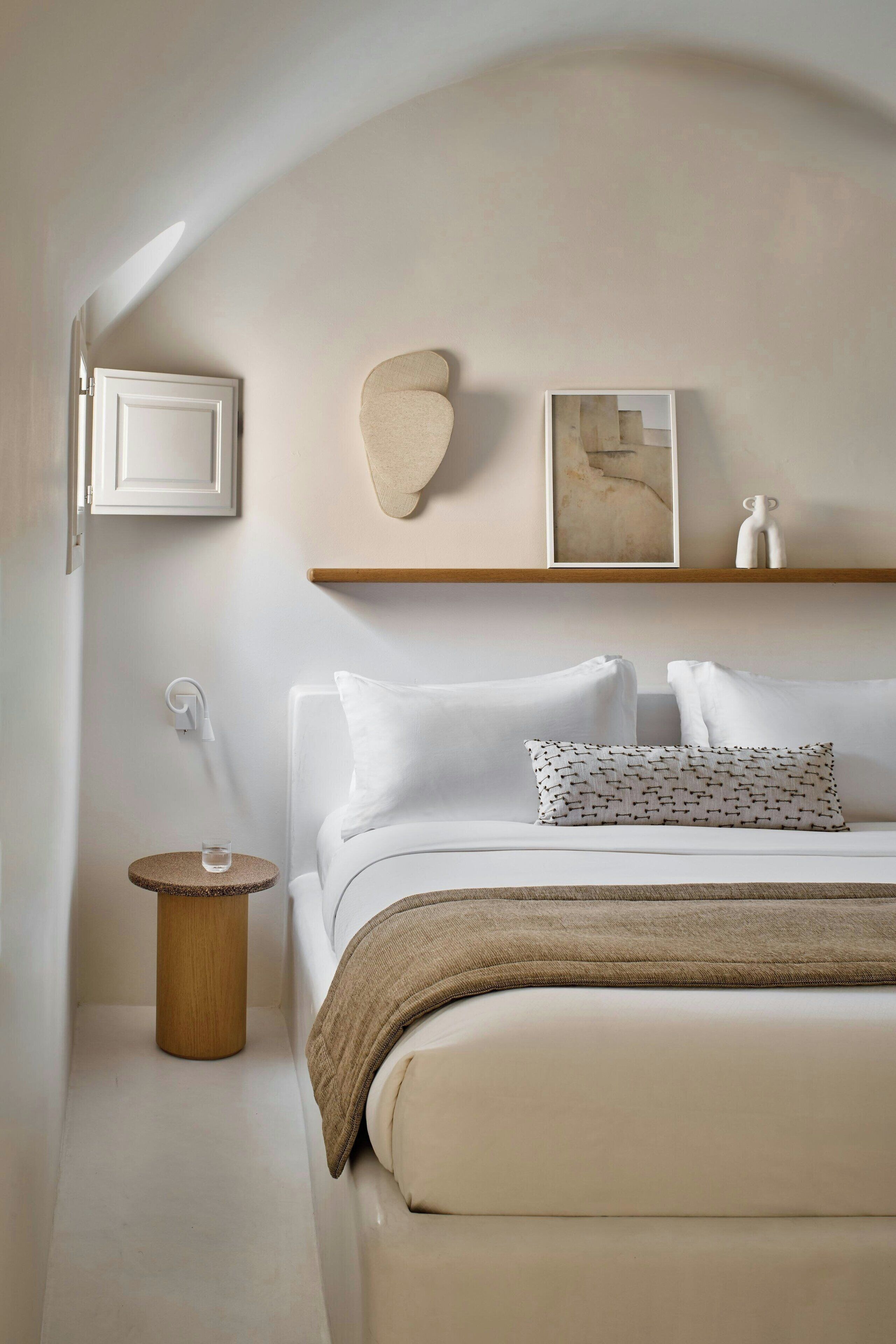 A minimalist bedroom with a bed, a bedside table, a wall-mounted shelf, and a framed picture.