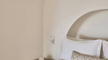 A neatly arranged bedroom with a curved ceiling, a bed with white linens, a patterned pillow, and a small round table with a white object.