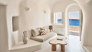 A modern living room with a sofa, a coffee table, and a view of the sea through an arched doorway. - Mystique, a Luxury Collection Hotel, Santorini (Santorini)