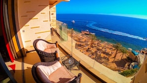 Ein Balkon mit Korbstühlen, einer Glastrennwand und Blick auf das Meer mit Booten und einem Strandabschnitt.