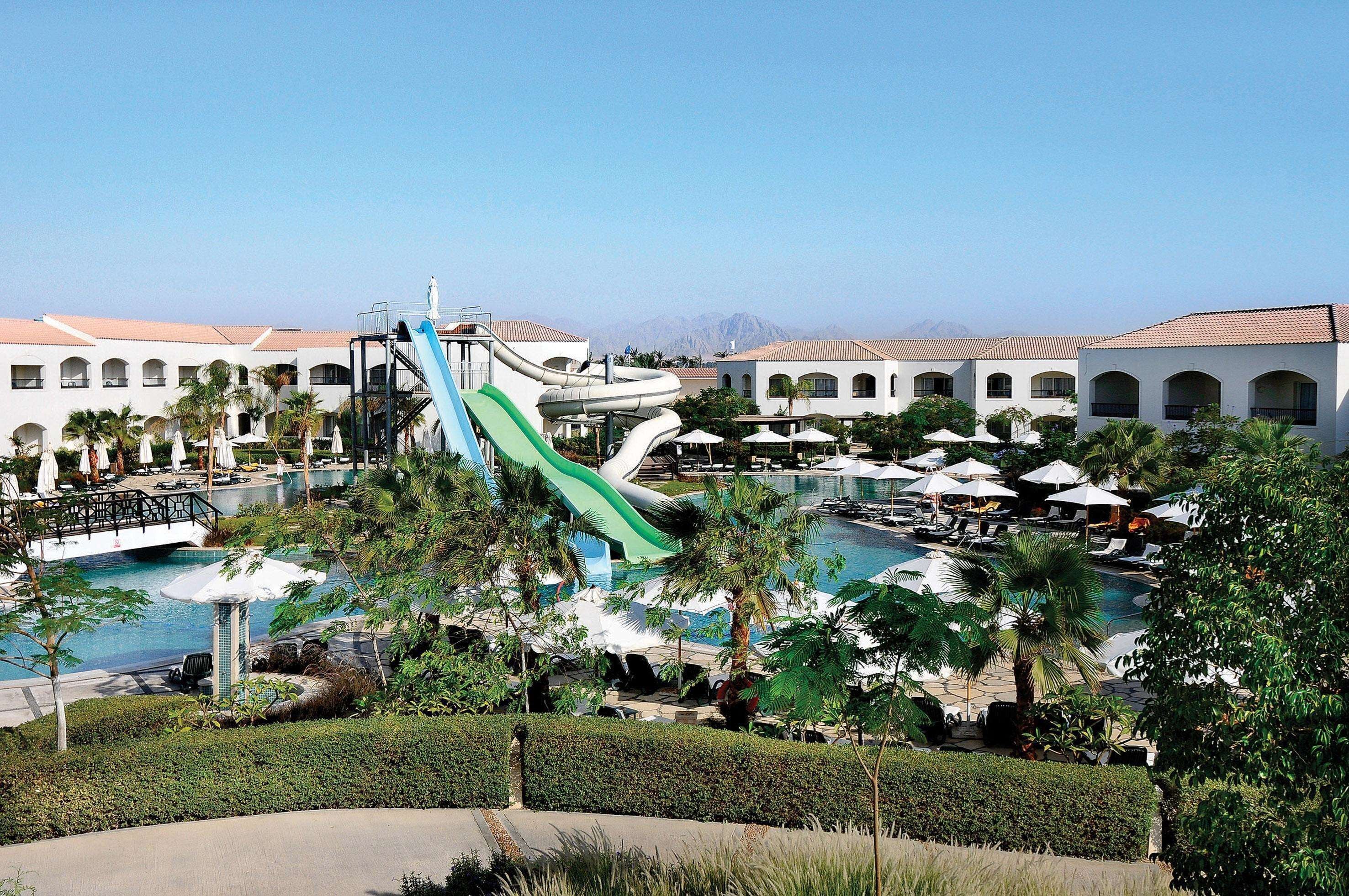 A resort with a water slide, swimming pool, and multiple lounge areas with umbrellas.