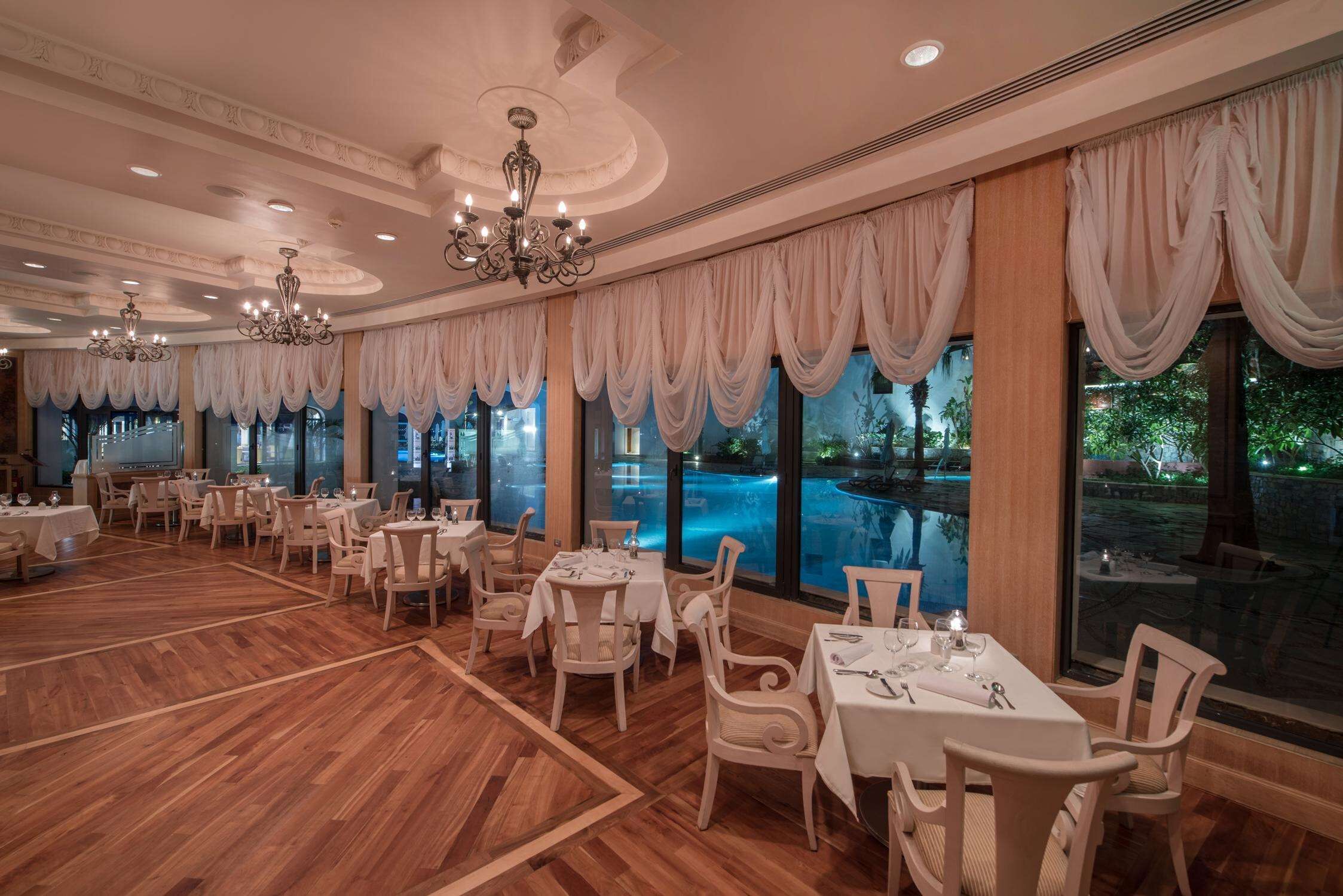 A restaurant with a pool view, wooden flooring, and elegant chandeliers.