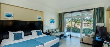 Une chambre d’hôtel avec deux lits, un canapé, une télévision et un balcon donnant sur un espace verdoyant.