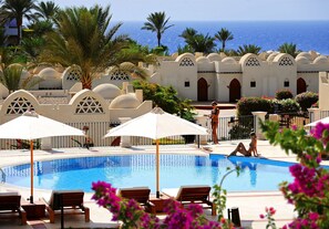 A pool area with lounge chairs and umbrellas, palm trees, and a view of the sea. - Reef Oasis Beach Aqua Park Resort - All inclusive (Sharm El Sheikh)