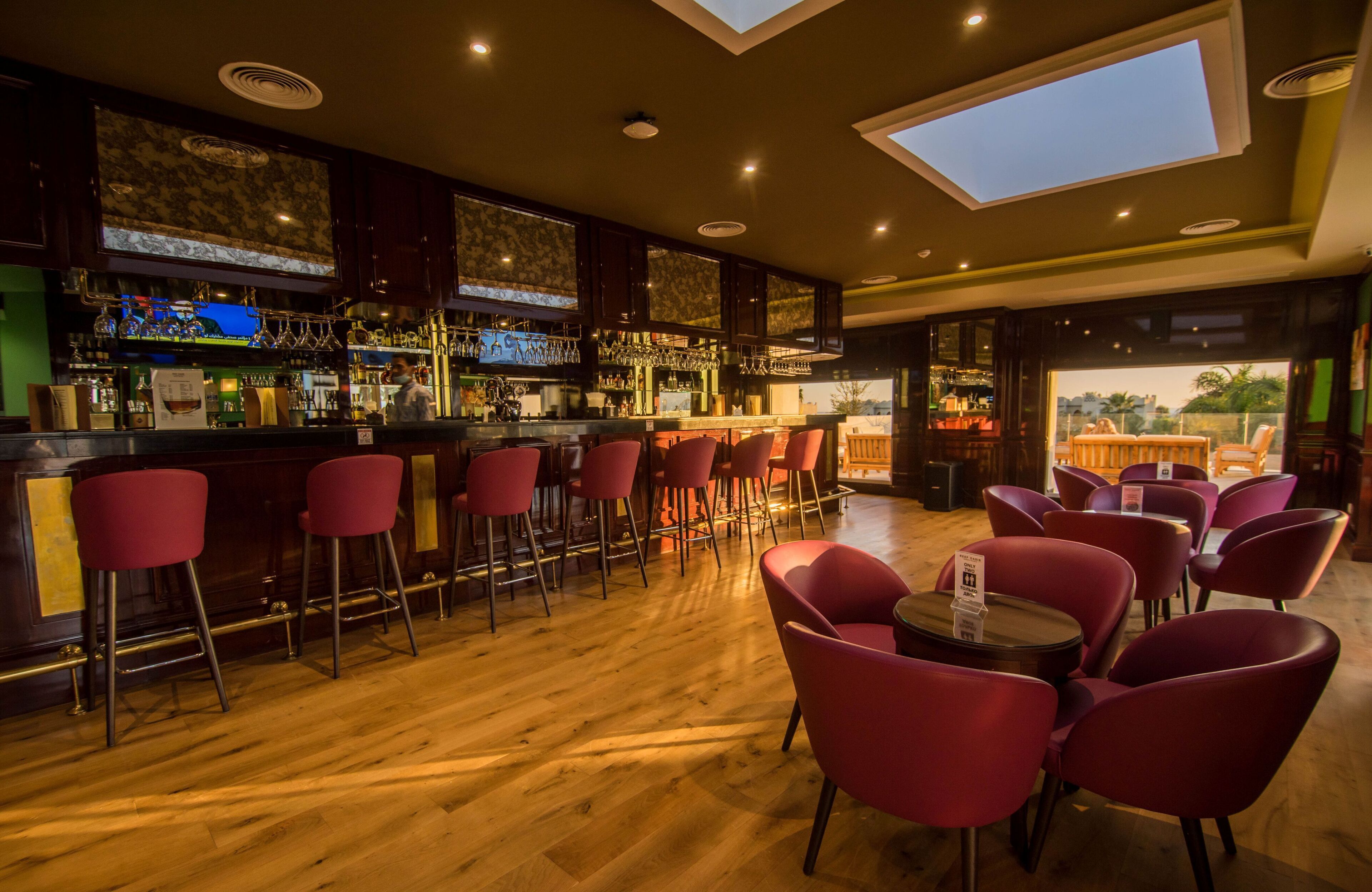 A bar area with wooden flooring, red bar stools, and a bar counter with various bottles and glasses.