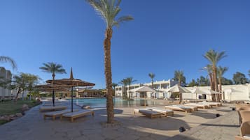 A poolside area with lounge chairs, palm trees, and umbrellas.