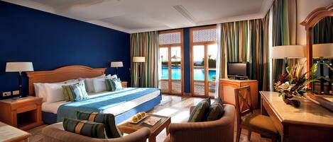 Une chambre d’hôtel avec un grand lit, un bureau avec une télévision, une chaise et une vue sur une piscine.
