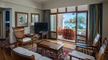 Amplia sala de estar con mobiliario de mimbre, televisor de pantalla plana y vista a una piscina y palmeras.