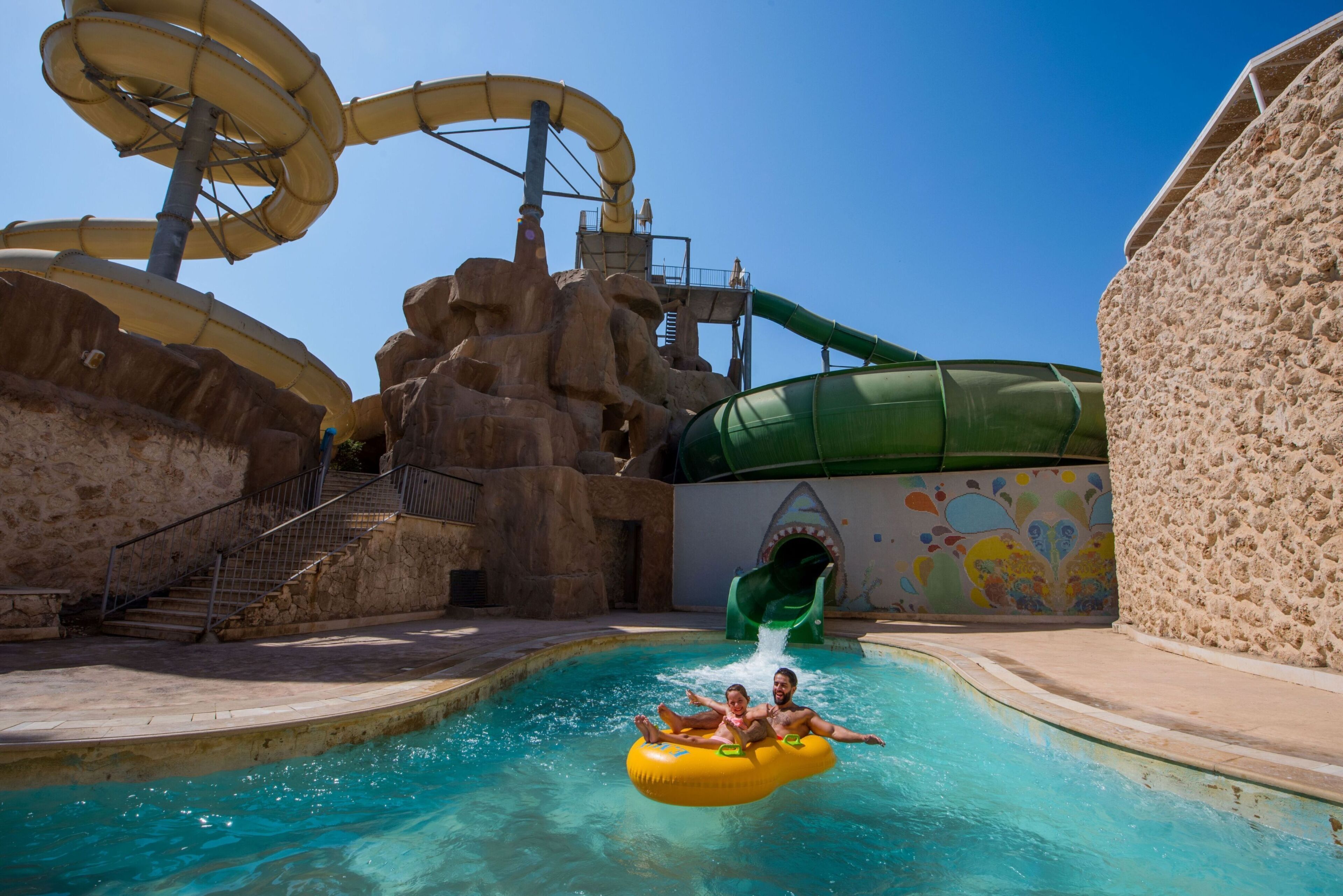 Un parque acuático con piscina, toboganes y una formación rocosa.