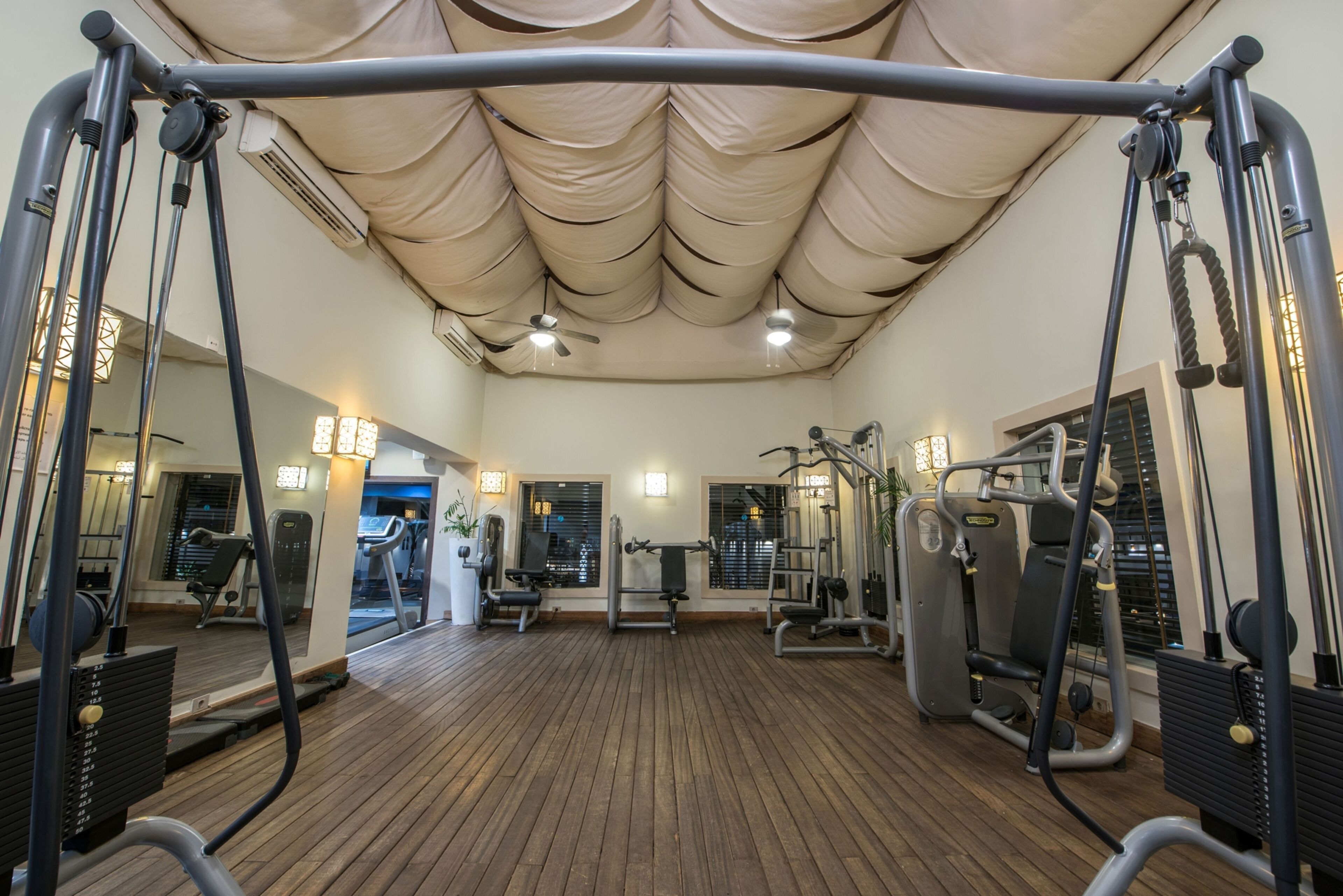 A gym with exercise equipment, a wooden floor, and a ceiling with a fabric canopy.