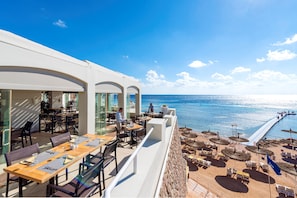 Un restaurante frente al mar con terraza y mesas y sillas, ofreciendo vistas a la playa.