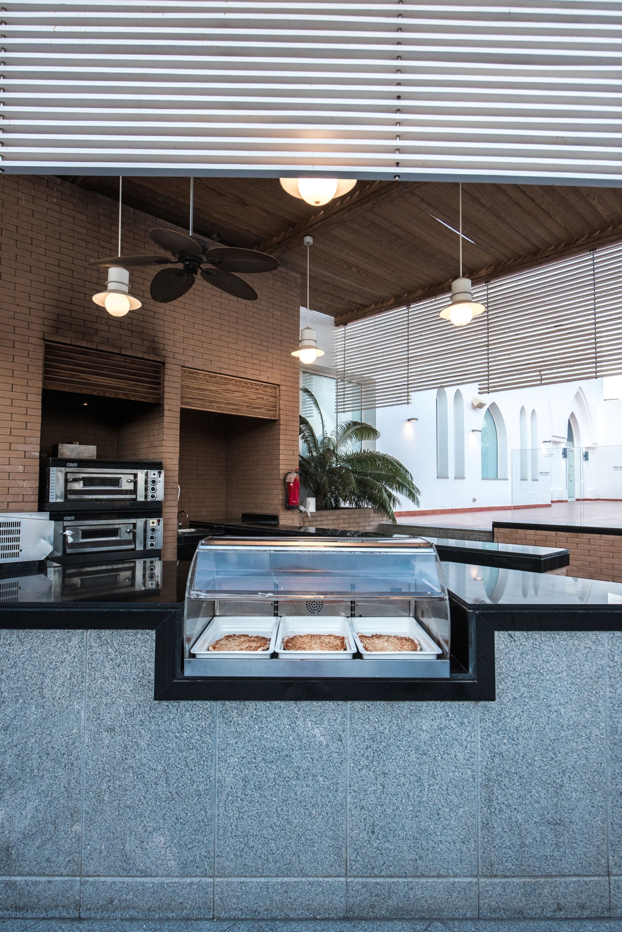 An outdoor seating area with a brick wall, ceiling fans, and a counter displaying baked goods.