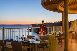 A restaurant with outdoor seating overlooking the sea, featuring wooden tables and chairs, and a waiter attending to guests. - Reef Oasis Beach Aqua Park Resort - All inclusive (Sharm El Sheikh)