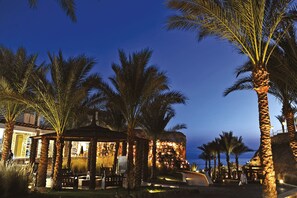 A well-lit outdoor area with palm trees and a building with a covered seating area. - Reef Oasis Beach Aqua Park Resort - All inclusive (Sharm El Sheikh)