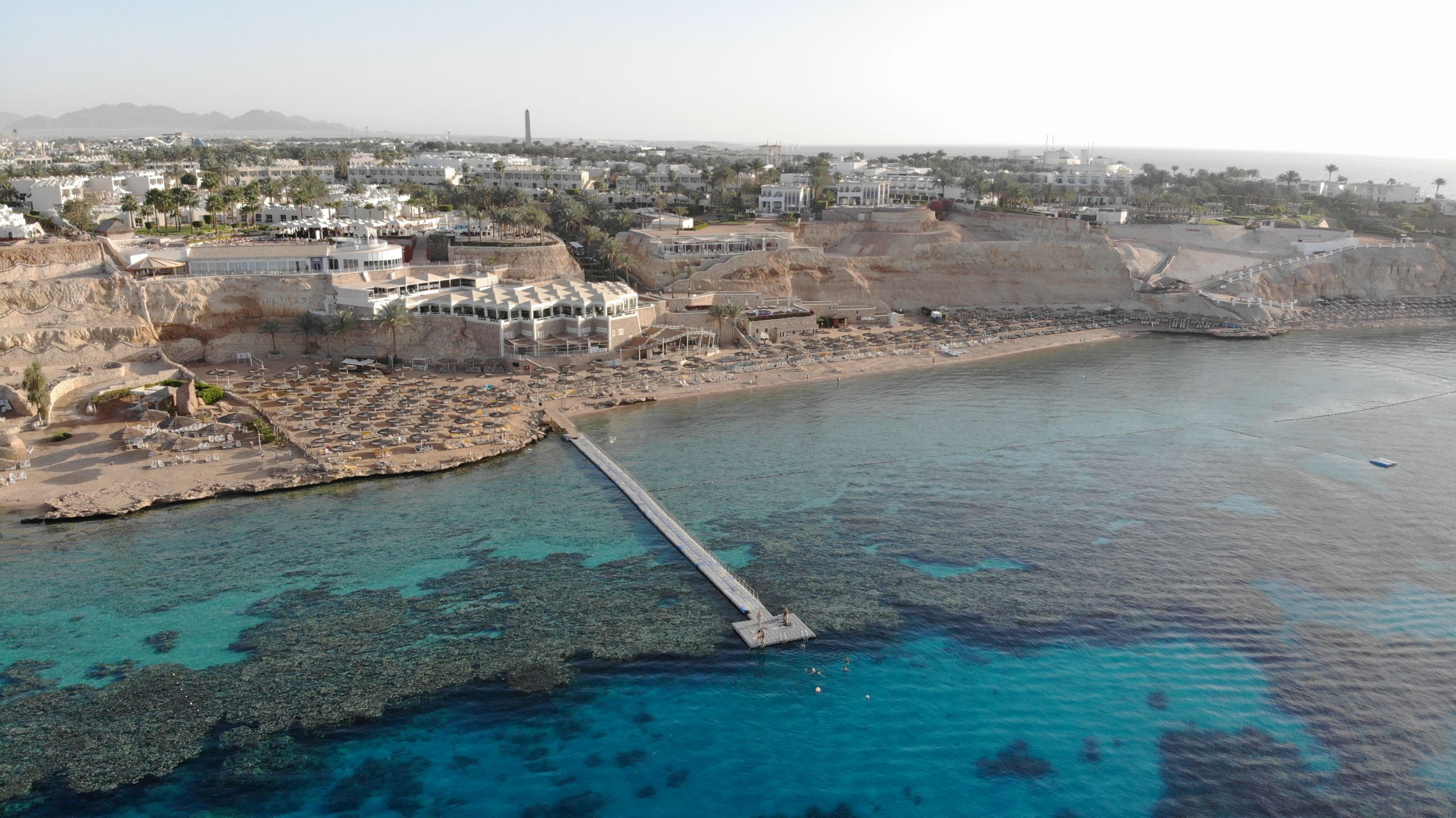 An aerial view of a coastal area with a pier extending into the water, surrounded by buildings and a beach.