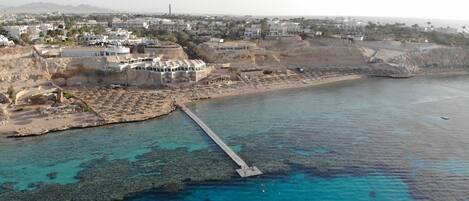 An aerial view of a coastal area with a pier extending into the water, surrounded by buildings and a beach.