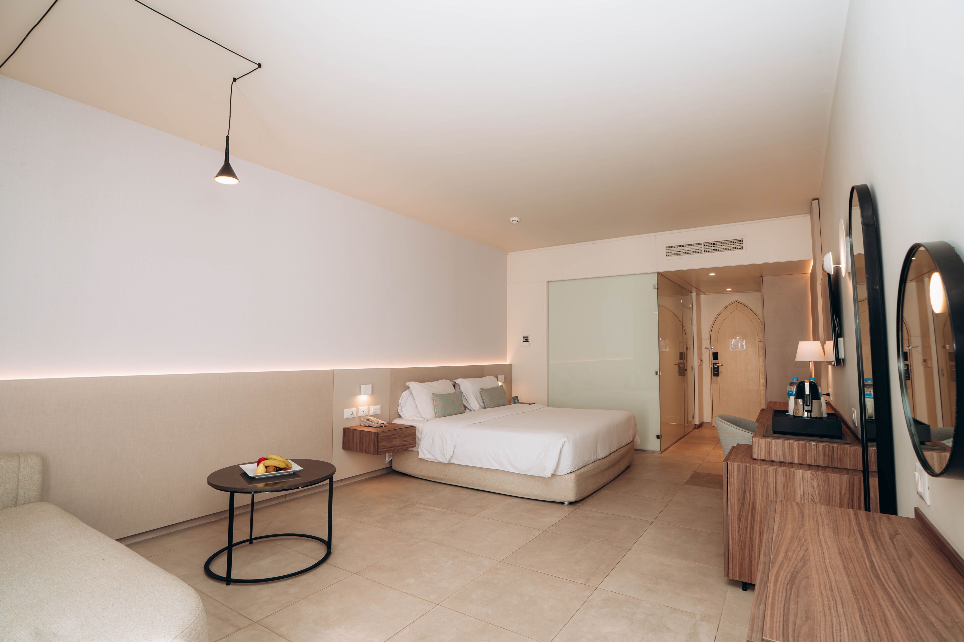 Una habitación de hotel moderna con una cama, mesita de noche y una pequeña mesa redonda con una lámpara.