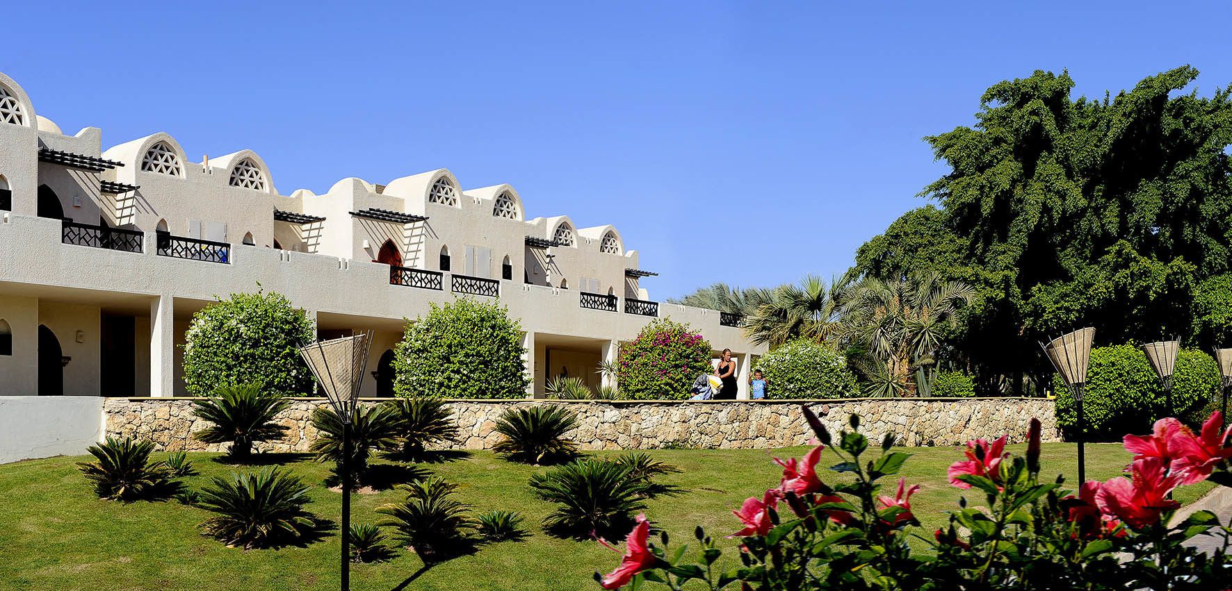 A hotel with multiple-story architecture, featuring balconies and a well-maintained garden with various plants and flowers.