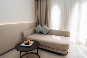 Una sala de estar moderna con un sofá beige, dos almohadas estampadas, una mesita redonda con una bandeja de frutas y cortinas de gasa.