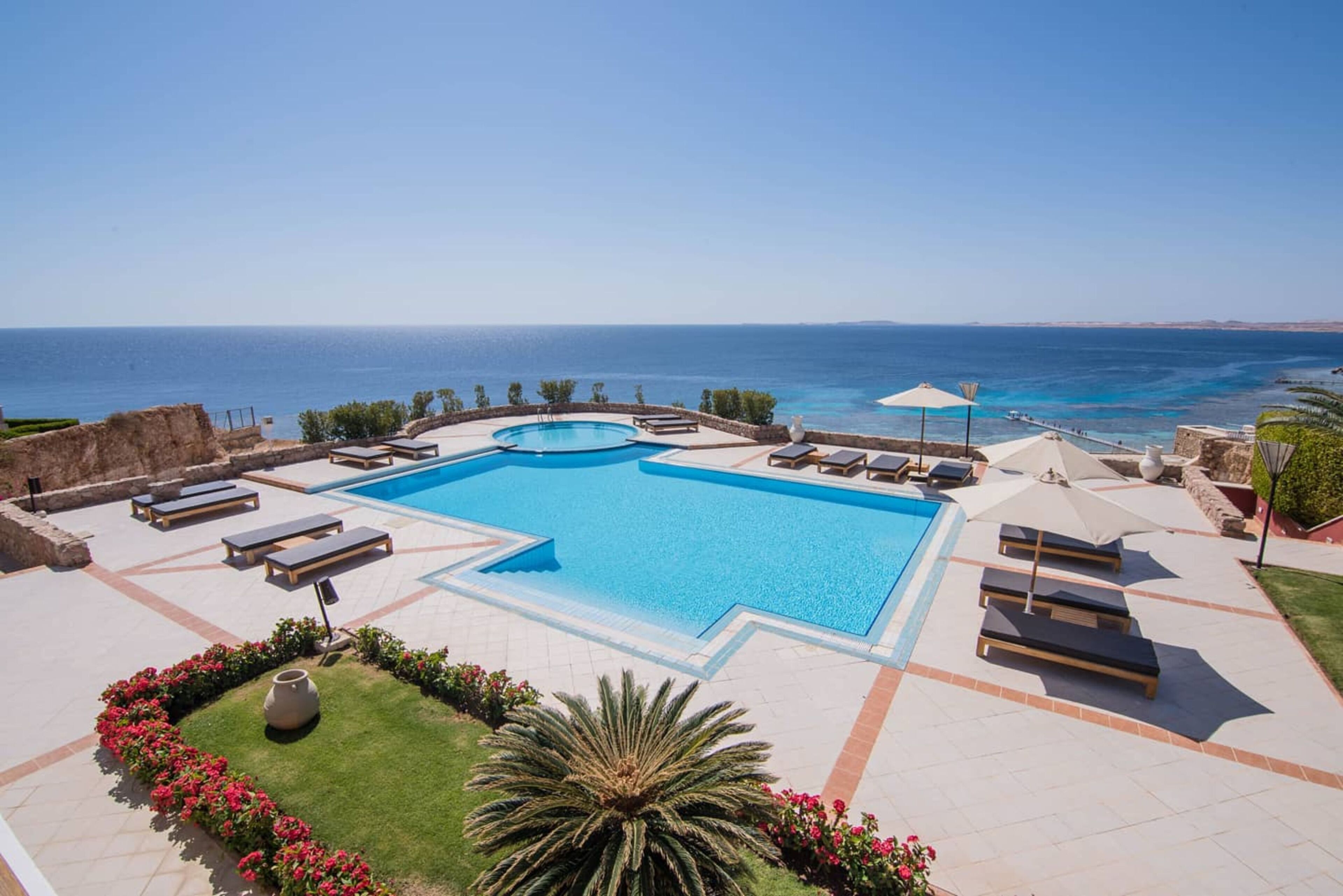 A pool with a view of the sea, surrounded by lounge chairs and umbrellas.