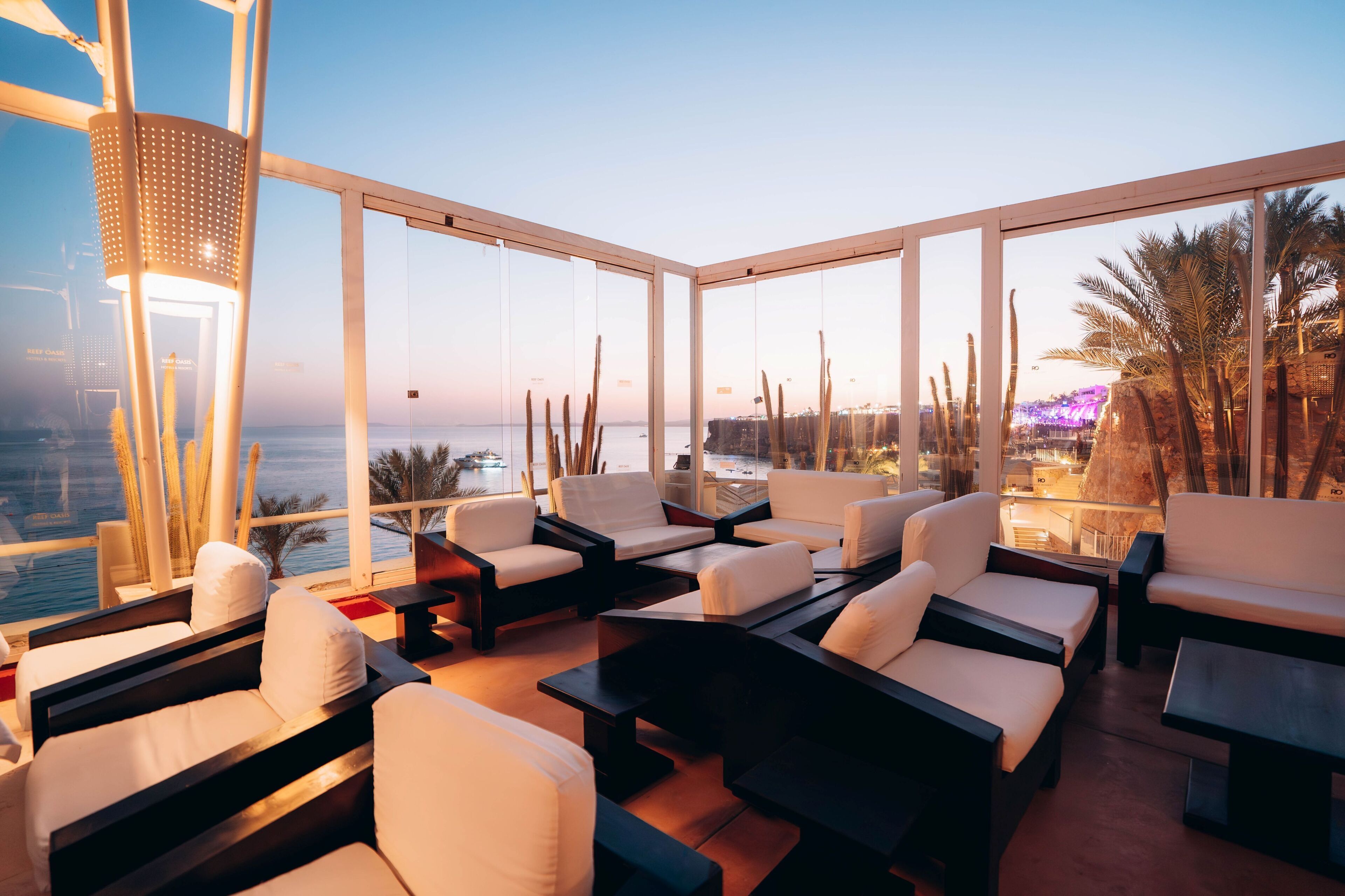 Eine moderne Lounge mit weißen Sofas und Tischen, große Fenster mit Blick auf das Meer und die Skyline.