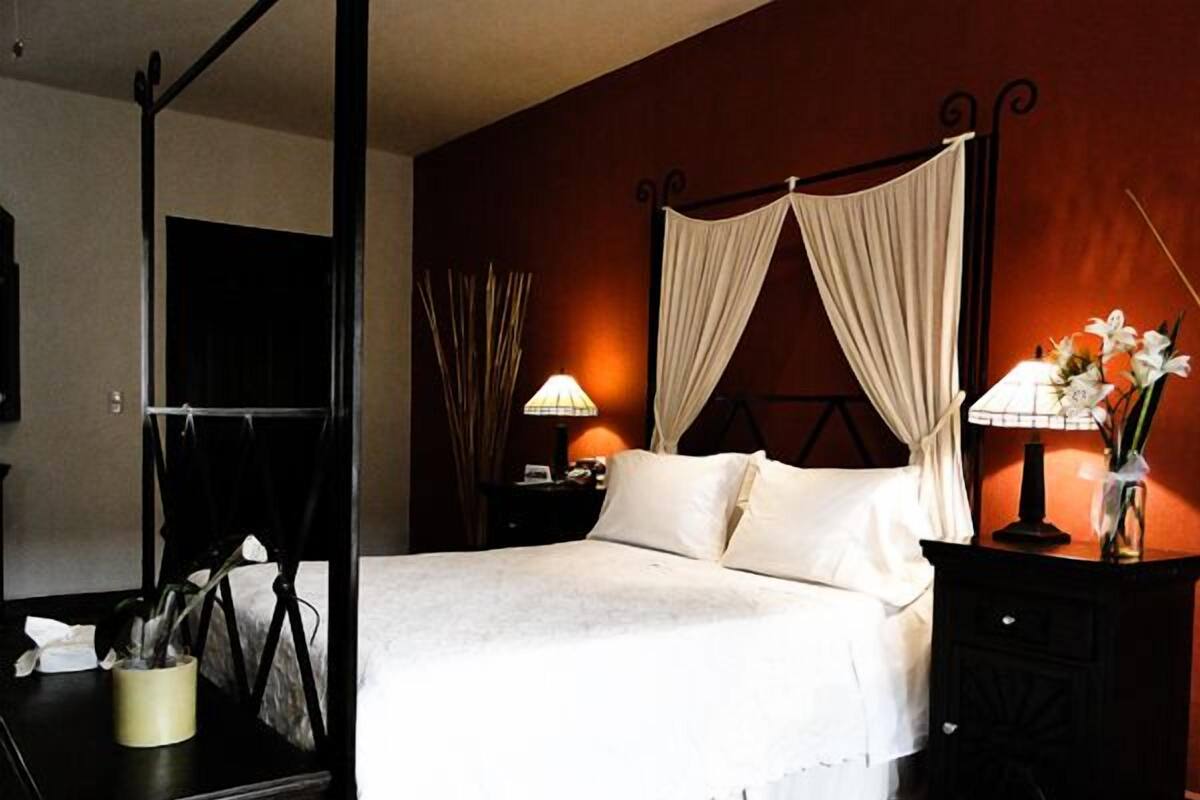 A hotel room with a bed, a nightstand, a lamp, and a vase with flowers.