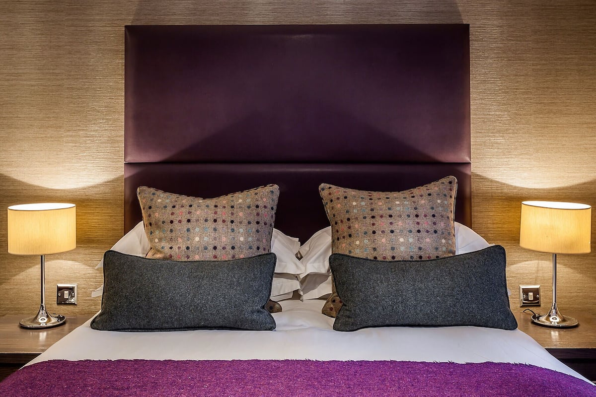 A bed with a dark headboard, two patterned pillows, and two bedside lamps.