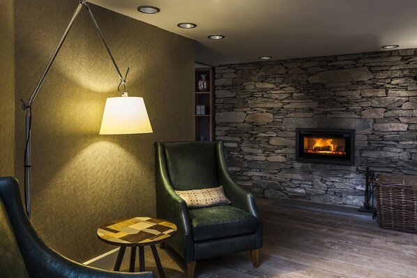 A cozy room with a stone wall, a fireplace, a green armchair, and a floor lamp.