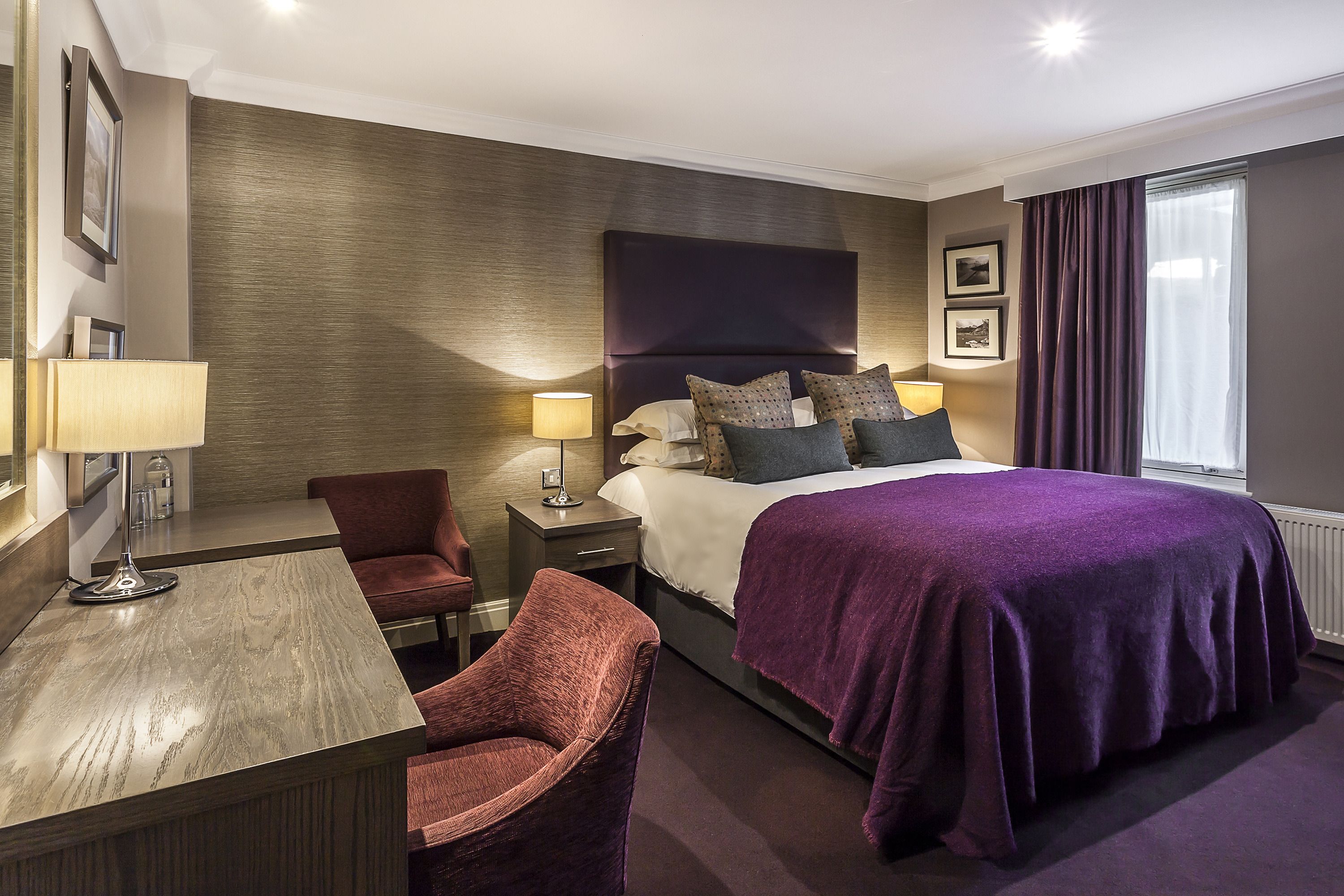 A hotel room with a large bed, a desk with a lamp, a chair, and a nightstand.