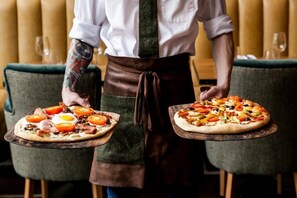 A person serving two pizzas on wooden boards. - The Langdale Hotel & Spa (Ambleside)